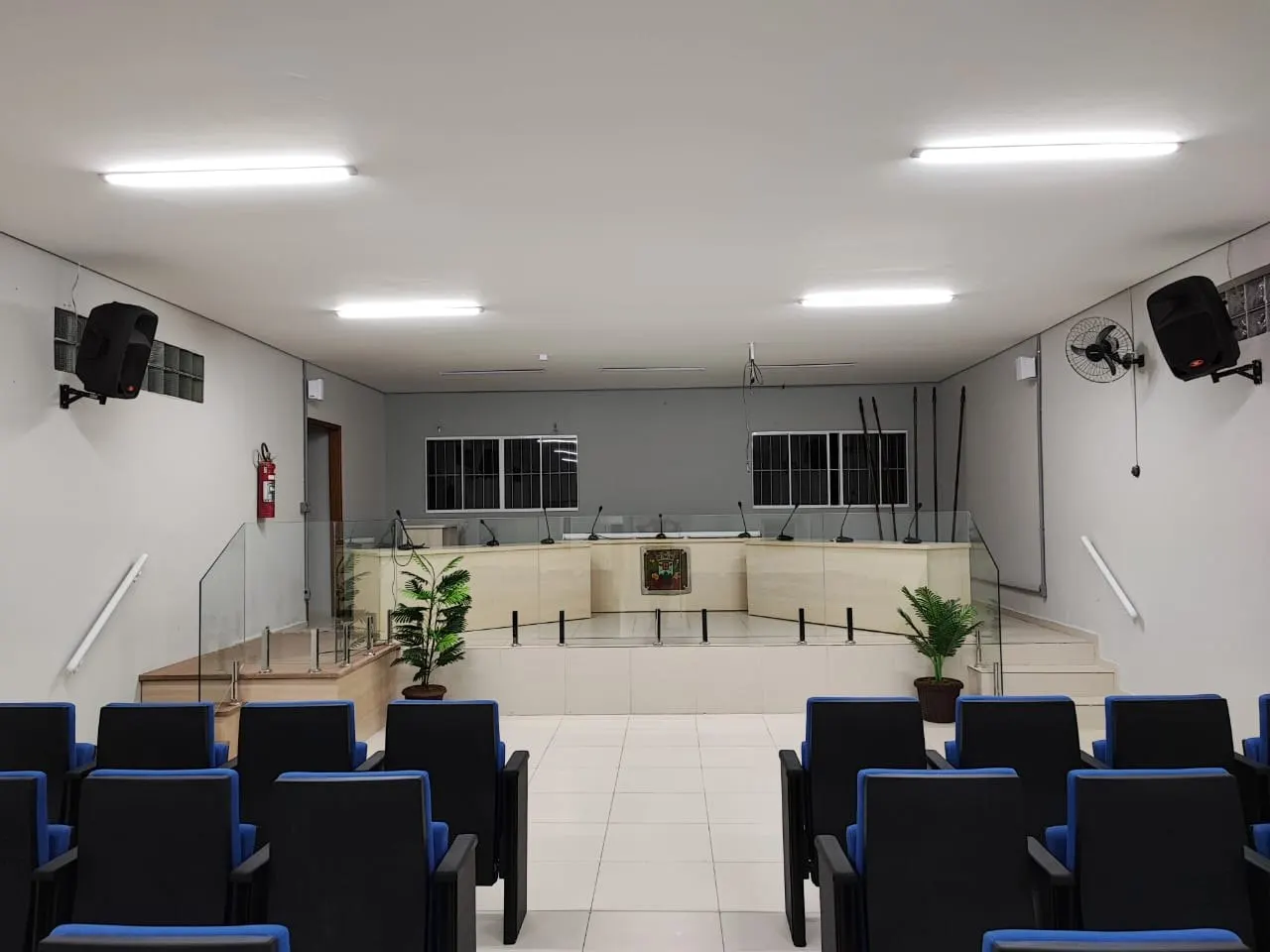 Plenário com mesa diretora, cadeiras e paredes em cinza-claro