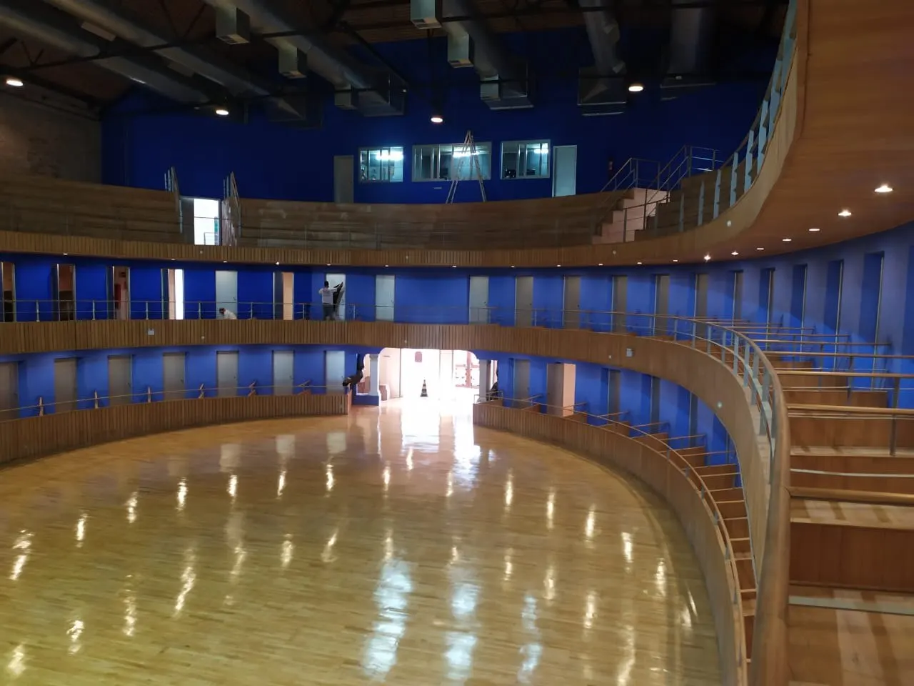 Galerias curvas com paredes azuis e piso de madeira durante a obra, sem cadeiras