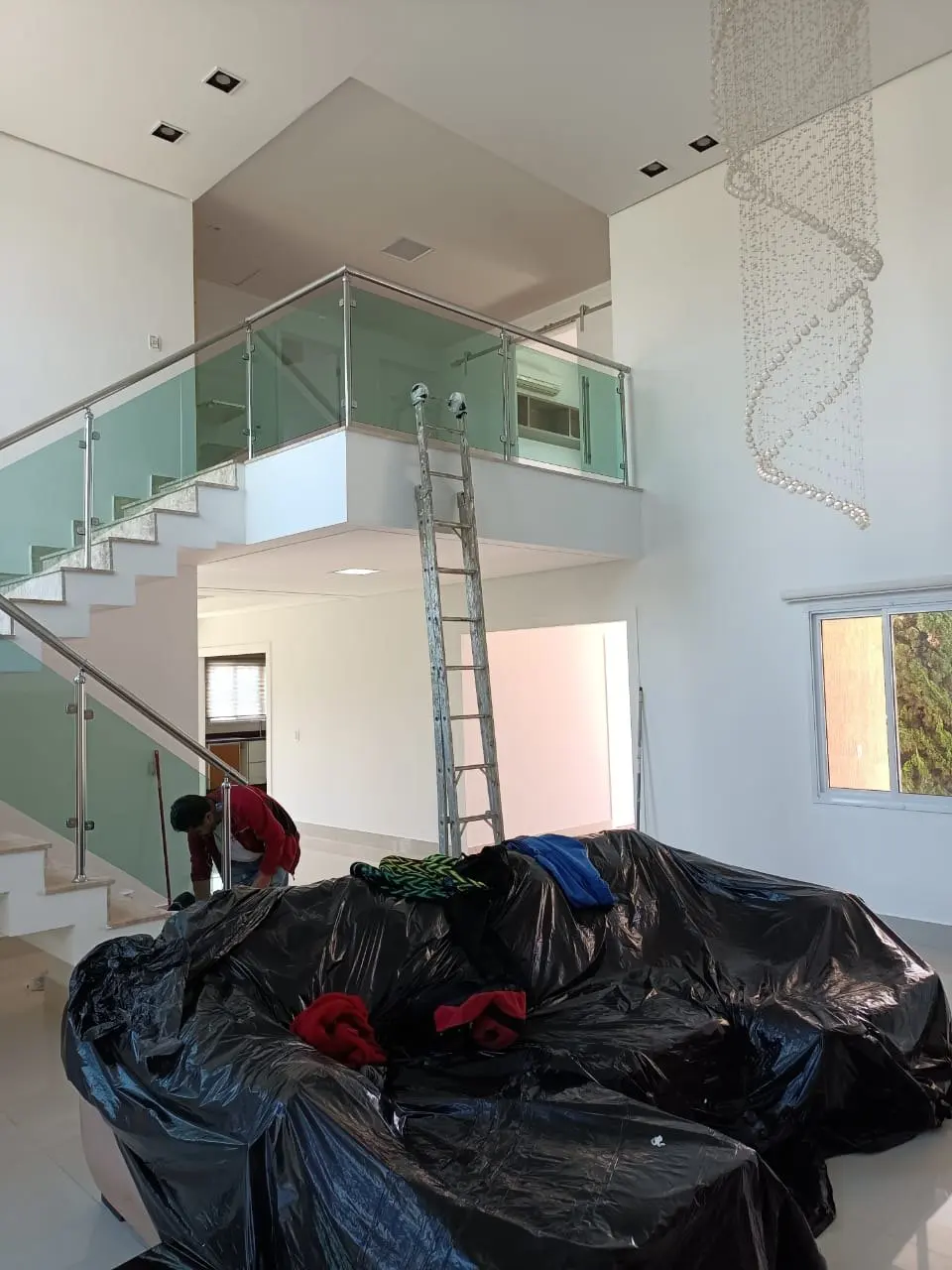 Móveis cobertos por lona preta enquanto o pintor trabalha no pé-direito duplo